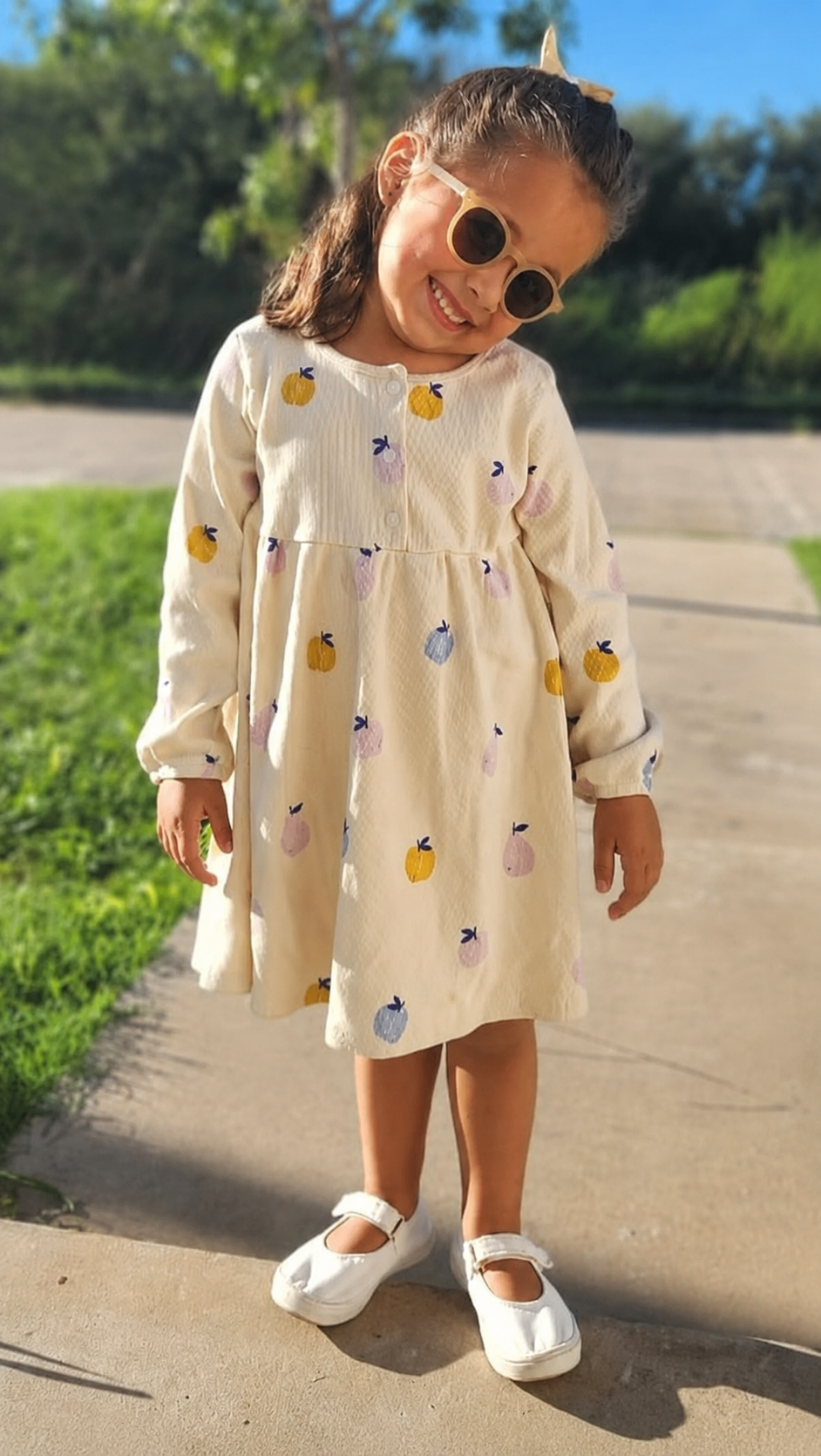 Niña con vestido y zapatitos blancos en el frente de su casa usando unos anteojos para niño.